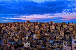Amman's pale stone buildings stacked across its hills under a blue sky